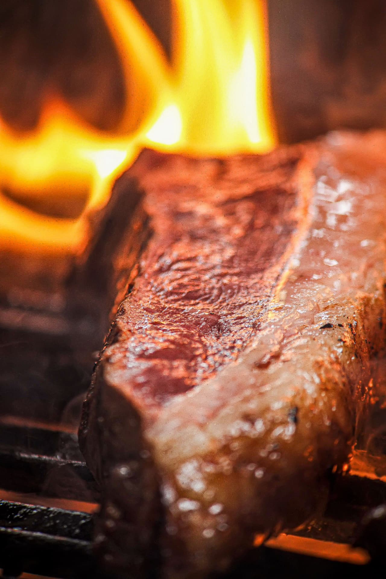 Corte de picanha assando na brasa com chamas ao fundo